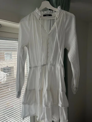 Volangklänning BikBok - Säljer den här  vita kortklänning från BikBok med volanger, knappar framtill och knytband vid halsen. Använd en gång och super bra skick!🤍