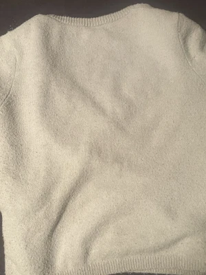 Grå omlott tröja från Kappahl  - Mysig ljusgrå omlottkofta från Kappahl i stickad kvalitet. Koftan har v-ringning, ribbade kanter och knytband i sidan för en snygg detalj. Perfekt för lager på lager under höst och vinter.