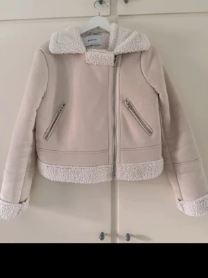 Beige teddyjacka från Stradivarius - Supermysig beige teddyjacka från Stradivarius med fluffigt foder och detaljer i fårskinnsimitation. Jackan har dragkedja framtill, två snedställda fickor med dragkedja och bred krage. Perfekt för kalla dagar och riktigt snygg till jeans eller kjol.