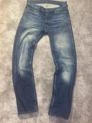 Faded Jeans - Säljer ett par feta jeans i blå tvätt med snyggt slitna detaljer på framsidan. Rak passform och femficksmodell med knappgylf. Tillverkade i tåligt jeanstyg som ger en tidlös look. Perfekta för dig som gillar en avslappnad och autentisk stil.