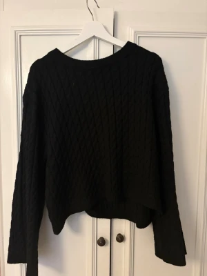 Svart stickad tröja från H&M - Mysig svart stickad tröja från H&M i storlek M. Tröjan har ett diskret kabelstickat mönster, rund halsringning och långa ärmar. Perfekt för lager på lager under kyliga dagar och enkel att matcha med jeans eller kjol.
