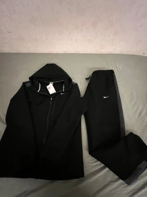 Svart Nike huvtröja med dragkedja - Säljer en svart huvtröja från Nike med dragkedja framtill och justerbar huva. Tröjan har en enkel och stilren design med Nike-logga på bröstet. Perfekt för dig som gillar sportig och clean stil.