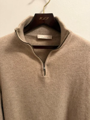 Luca Faloni zip - Säljer en supermjuk beige kashmirtröja från Luca Faloni med half zip och hög krage. Tröjan är långärmad och har en clean, klassisk look som är lätt att matcha. Perfekt för dig som gillar stilrena och bekväma plagg.