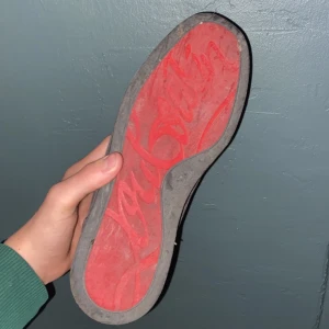 Grå mockasneakers från Christian Louboutin - Säljer ett par grå sneakers från Christian Louboutin med klassisk röd sula och snygg mocka. Skorna har rund tå, snörning och diskreta detaljer i samma ton. Insidan är i ljust skinn och det står 'Paris' tryckt i hälen. Perfekta för dig som gillar lyxiga och stilrena sneakers.