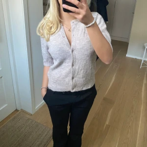 Beige stickad kofta  - Superfin beige stickad kofta med korta ärmar och v-ringning. Koftan har knappar framtill och ribbade muddar vid ärmslut och nederkant. Perfekt att slänga på sig över ett linne eller t-shirt för en chill och stilren look. Använd 1-2 ggr🥰🥰