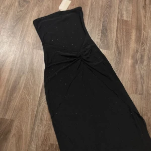 Maxiklänning med detaljer från meshki  - Supersnygg svart axelbandslös långklänning från Meshki med svarta strass detaljer och twistad knut framtill, storlek M