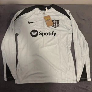 Barça långärmad Nike fotbollströja S - Snygg långärmad fotbollströja från Nike för FC Barcelona i ljusgrått med svarta detaljer på axlar och ärmslut. Tröjan har klubbmärke, Nike-logga och Spotify som sponsortryck på bröstet. Tillverkad i lätt och ventilerande Dri-FIT-material.