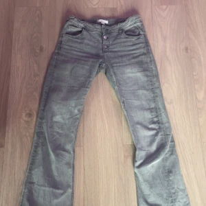 Grå utsvängda jeans - Gråa lågmidjade bootcut jeans från Gina tricot. Säljer då dom blivit för små på mig men har använt mycket innan det, de är inget som syns. Byxorna har tre knappar framtill och inget mönster på fickorna.
