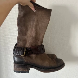 Bruna bikerboot med spänne - Säljer ett par bruna boots i skinn med robust klack och coolt mörkbrunt bälte med dubbla spännen runt ankeln. De har rund tå och en slitstark sula, från märket Airstep köpta för 800kr säljs då det tyvärr är för stora 😩