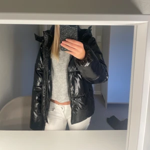 Svart pufferjacka från Nelly XS - Säljer en svart, glansig pufferjacka från Nelly i storlek XS. Använd 1 vinter, inga defekter. Jackan har huva och dragkedja framtill. Perfekt för kalla dagar när du vill ha en stilren vibe och ändå hålla värmen. Snygg och enkel att matcha med allt. Nypris 800 kr.