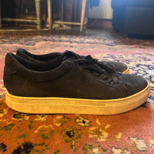 Vagabond Svarta mockasneakers med vit sula 42 - Snygga svarta sneakers i mocka med klassisk rund tå och platt, vit sula. Skorna har svarta snören och en stilren design som passar till det mesta. Perfekta för dig som gillar en clean och enkel look.