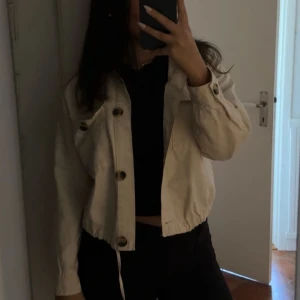 Beige croppad overshirt med knappar - Snygg beige croppad overshirt med stora knappar framtill och resår i midjan. Jackan har lång ärm och en avslappnad passform, perfekt att slänga över en t-shirt. Enkel och stilren design som passar till det mesta. Från bershka