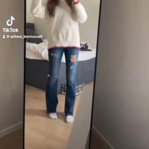 Blå bootcut jeans med slitningar - Säljer ett par blå jeans med bootcut-modell och snygga slitningar på låren och knäna. Jeansen har låg midja och klassisk femficksdesign. Materialet är jeans i bomull och de har en cool, avslappnad vibe.