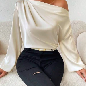 Offshoulder sidenblus i beige - Säljer en elegant offshoulder i beige siden med långärmad design. Blusen har en snygg draperad omlott-look över axlarna och är riktigt mjuk och glansig. Perfekt för dig som gillar stilrena och trendiga toppar med lite extra lyxig känsla.