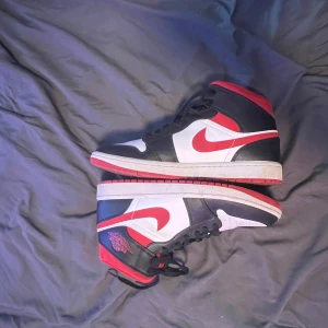 Nike Air Jordan 1 High svart/röd/vit st 43 - Säljer ett par Air Jordan 1 High i svart/vit/röd färgkombination. Skorna är använda men fortfarande i bra skick. St 43