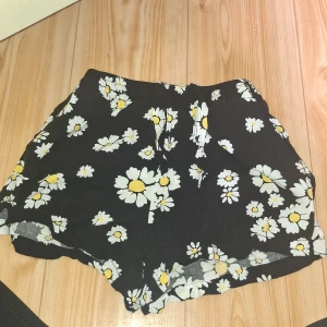 Svarta blommiga shorts från Stay - Snygga svarta shorts från Stay med ett gulligt blommigt mönster i vitt och gult. Modellen är loose fit med elastisk midja och snörning framtill. Perfekta för varma dagar och chill häng. Materialet känns lätt och luftigt.