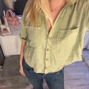 Grön kortärmad skjorta från Zara - Ljusgrön skjorta från Zara med korta ärmar, två bröstfickor och träfärgade knappar framtill. Fint skick!