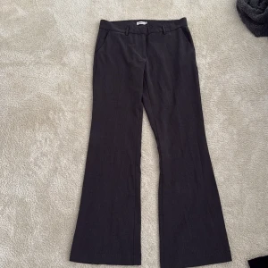 Mörkgrå kostymbyxor med bootcut - Snygga mörkgrå kostymbyxor med bootcut och klassiska fickor fram och bak. Byxorna har hällor för bälte och är tillverkade i ett vävt material som ger en dressad look. Perfekta för dig som gillar stilrena och tidlösa plagg. Litet slitage på ena fickan men det är inget som syns om man inte drar i fickan 