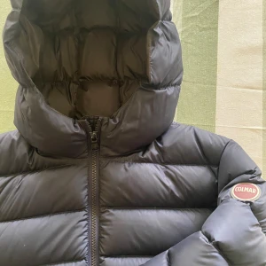 Mörkblå Colmar pufferjacka med huva - Säljer en mörkblå pufferjacka från Colmar med huva och två dragkedjeförsedda fickor. Jackan är fylld med naturligt dun och har en klassisk quiltad design. Perfekt för kalla dagar och riktigt snygg streetstil. Inköpt förra hösten för 4499:-  (kvitto finns)