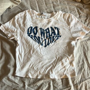 Vit t-shirt med blå text från FB Sister/ New Yorker - Vit t-shirt från FB Sister i bomull med blått tryck på bröstet där det står 'Do What You Love' i ett hjärtformat mönster. Klassisk rund hals och korta ärmar, cropad. Lite skyklig men går att stryka eller bara tvätta och hänga upp!! Liten fläck men syns inte!