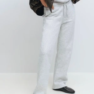 Mjukisbyxor ginatricot  - Snygga ljusgrå mjukisbyxor med raka ben och dragsko i midjan. Byxorna har en relaxed passform och är tillverkade i mjukt bomullsmaterial. Perfekta för chill dagar eller när du vill vara extra bekväm.