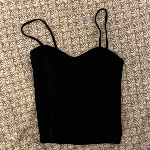 Svart korsettopp från Gina Tricot - Säljer en svart korsettopp från Gina Tricot med smala axelband och markerade kupor. Toppen har en figurnära passform och är tillverkad i ett mjukt material. 😊👍🏼