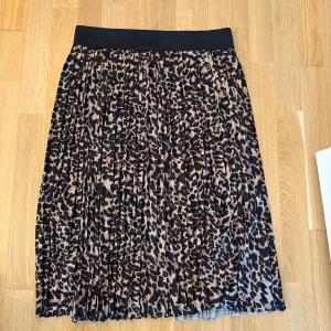 Leopard kjol  - Leopardmönstrad plisserad kjol med svart resår i midjan. Kjolen har en elegant och tidlös design som passar perfekt för både vardag och fest. Storlek 38