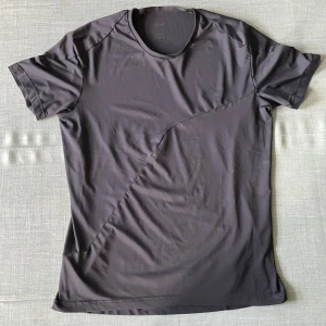 Svart tränings t-shirt från Adidas - Snygg svart tränings t-shirt från Adidas med diskret logga på bröstet. T-shirten har korta ärmar, rund halsringning och är tillverkad i ett mjukt och lätt polyestermaterial. Perfekt för dig som gillar en stilren och sportig look.