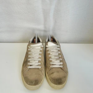 Saint Laurent beige mockasneakers - Snygga sneakers från Saint Laurent i beige mocka med vit sula och vita skosnören. Sidan pryds av handskriven logga. Skorna har en klassisk låg profil och rund tå, perfekt för en clean och avslappnad look. Pris kan sänkas vid snabb affär💯😁