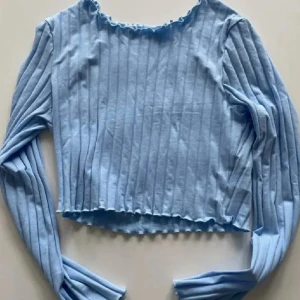 Ljusblå ribbad topp från SHEIN XS - Säljer en ljusblå långärmad topp från SHEIN i storlek XS. Toppen är ribbad med smalrandigt mönster och har en croppad passform med vågig kant vid hals och nederdel. Materialet är mjuk bomull med lite stretch för extra komfort.