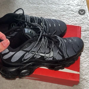 Nike Air Max svarta sneakers strl 43 - Svarta Nike Air Max sneakers med grå och silvriga detaljer. Ovandel i mesh och syntet, med tydlig Nike swoosh på sidan. Skorna har snörning och en robust, synlig Air Max-sula som ger en sportig vibe. Perfekta för dig som gillar streetwear och bekväma skor.