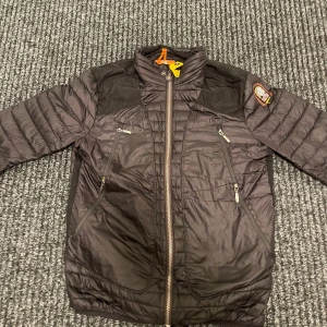 Svart pufferjacka från Parajumpers S - Snygg svart pufferjacka från Parajumpers i storlek S. Jackan har quiltad design, hög krage, flera dragkedjefickor och coolt patch på ärmen. Lätt och smidig med orange detaljer på insidan. Perfekt för dig som vill ha en stilren och sportig look. PRIS KAN DISKUTERAS