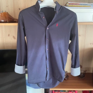 Mörkblå Polo Ralph Lauren skjorta - Mörkblå skjorta från Polo Ralph Lauren. Bra passande modell med mönstrad insida på krage och ärm. Den är i bomull och är i bra skick. Vid funderingar så är det bara att fråga. 