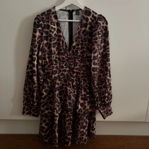 Leopardmönstrad klänning med v-ringning - Säljer en snygg kortklänning med leopardmönster. Klänningen har v-ringning, långa ärmar. Materialet är mjukt och följsamt, perfekt för både vardag och fest. Dragkedja bak. Endast provad🐆