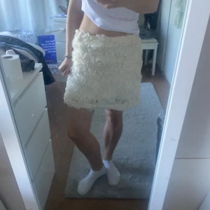 Vit blommig kortkjol  - Supersöt vit kortkjol från Kappahl med 3D-blommor över hela tyget. Kjolen har en rak passform och är täckt av mjuka tygrosor. Aldrig använd men tvättad en gång. 🩷