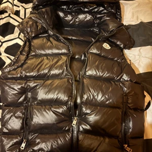 Svart dunväst från Moncler med huva - Hej säljer min moncler väst för att den blivit snäppet för liten för mig, inga skråmor på den, storlek 3 vilket motsvarar storlek m, den är som ny har påsen jag fick med den i tyvärr ej kvittot då jag fick den i födelsedagspresent för ett halv år sen