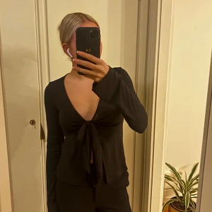 Svart omlottopp med knyt framtill - Svart långärmad omlottopp med djup v-ringning och knyt framtill. Strl S 