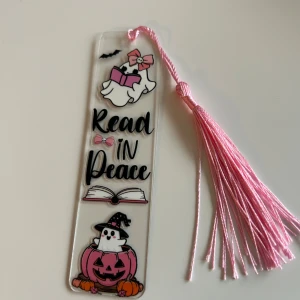 Read in Peace halloween bokmärken - Detta är ett bokmärke med gulliga spökfigurer, rosa detaljer och texten 'Read in Peace'. Perfekt för dig som älskar böcker med en touch av Halloween och vill ha något unikt och lekfullt till din läsning. Passar både ungdomar och  vuxna som vill göra läsningen lite roligare.
