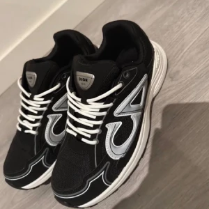 Svarta Dior B30 sneakers med silverdetaljer - Säljer ett par svarta Dior B30 sneakers med vita och silverfärgade detaljer. Skorna har en chunky vit sula, snörning och stora CD-loggor på sidorna och hälen. Ovandelen är i mesh och syntet med coola kontrastlinjer och en sportig vibe.