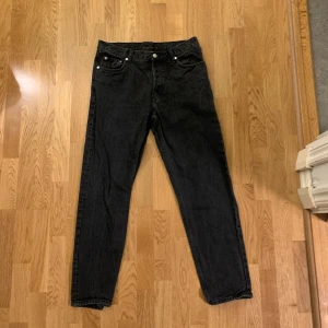 Svarta Weekday Barrel Relaxed jeans - Svarta jeans från Weekday i modellen Barrel Relaxed Tapered. De har en avslappnad passform med avsmalnande ben, klassiska fem fickor och knappgylf. Jeansen är tillverkade i bomull och har en stilren look som funkar till många olika outfits.