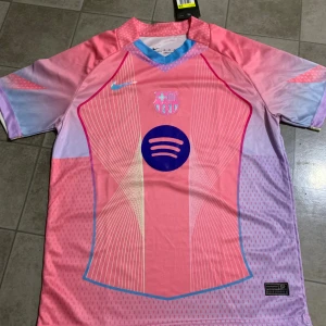 Rosa FC Barcelona fotbollströja Nike - Säljer en riktigt snygg FC Barcelona fotbollströja från Nike i rosa och ljuslila med coola grafiska linjer och Spotify-logga på bröstet. Kortärmad modell i lätt, ventilerande Dri-FIT material. Matchande shorts med Barca-emblem och Nike-logga ingår.