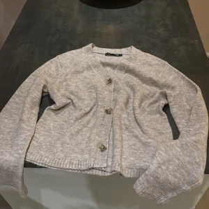 Beige stickad kofta med knappar - Mysig beige stickad kofta från lager 157 med tre stora knappar framtill. Koftan har v-ringning, lång ärm och ribbade muddar. Perfekt att slänga på sig över en t-shirt eller linne för en chill look.💞💞