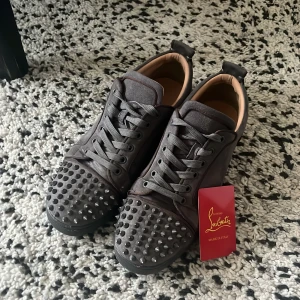  Christian Louboutin skor - Säljer ett par grå sneakers från Christian Louboutin med snörning och coola nitar på tån. Skorna har rund tå och platt sula, tillverkade i skinn med en mörkgrå ton. Perfekt för dig som vill sticka ut med exklusiva detaljer.