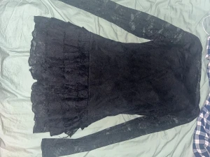 Svart spetsklänning med volang - Svart kortklänning med långa ärmar i transparent spets. Kjolen har flera lager volanger som ger en cool och feminin vibe. Klänningen är figurnära och har en snygg struktur i spetsmaterialet. Perfekt för dig som gillar att sticka ut med detaljer.