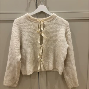 Beige stickad tröja med knyt från Gina Tricot - Supermysig beige stickad tröja från Gina Tricot med snygga rosetter framtill. Tröjan har långärmad design, ribbad struktur och rund halsringning. Perfekt för vintern då den är varm och skön❄️