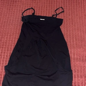 Svart kort klänning med smala axelband - Svart klänning från Monki med smala axelband och enkel, rak passform. Kort längd och stilren design som funkar till många olika looks. Materialet är mjukt och lätt, perfekt för varmare dagar. Snygg att styla med sneakers eller boots.