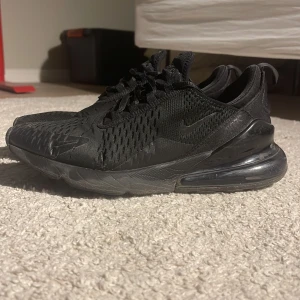 Nike Air Max 270 helsvarta sneakers - Nike Air Max 270 sneakers i helsvart färg med mesh-överdel och synlig Air-enhet i hälen. Snygg sportig design med snörning och rund tå.                                    De har hål på några ställen på skorna och priset kan diskuteras. Skorna har lite repor.
