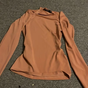 Beige långärmad topp från BikBok - Säljer en beige långärmad topp från BikBok i storlek XS. Toppen har en asymmetrisk halsringning med en cool detalj över ena axeln. Materialet är mjukt och stretchigt, vilket gör den riktigt skön att bära. Perfekt för dig som gillar stilrena plagg med en twist.
