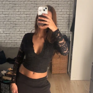 Spetströja  - Långärmad tröja i spets och urringning. Blusen har en djup v-ringning och är croppad i modellen. Storlek xs 