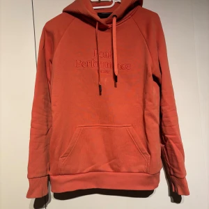 hoodie från Peak Performance - Säljer en snygg korallfärgad hoodie från Peak Performance med broderad logga på bröstet. Tröjan har huva med snörning, behövs en tvätt